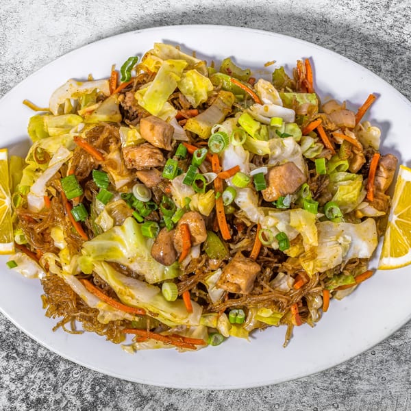 Filipino Pancit Bihon with chicken, cabbage, carrots, and green onions, garnished with lemon wedges.