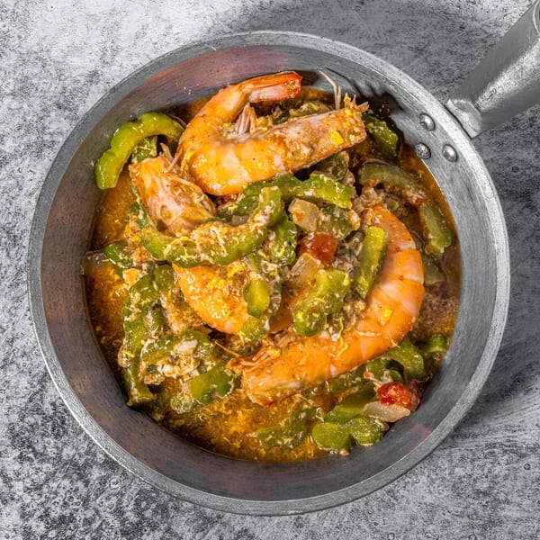 Filipino shrimp and bitter melon in a savory sauce, served in a metal pan.