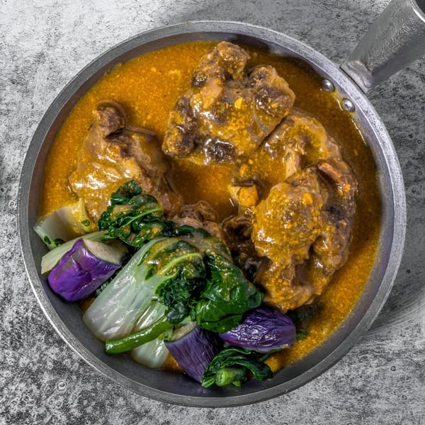 Adobolicious Kare-Kare, a Filipino stew with meat, peanut sauce, bok choy, and eggplant in a pan.