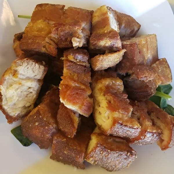 A close-up of golden-brown, crispy fried pork belly pieces, known as Adobolicious Bagnet, on a white plate.