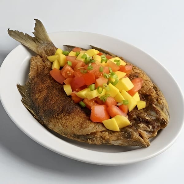 Crispy fried fish topped with diced tomatoes, mangoes, and green onions on a white oval plate.