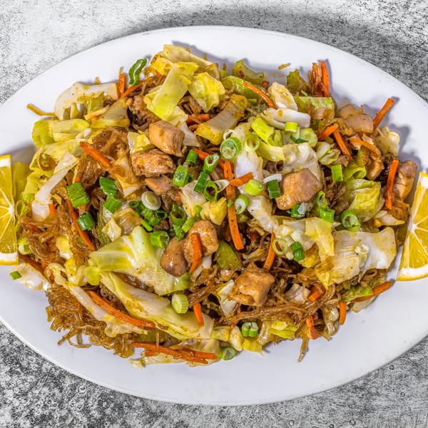 Adobolicious Pancit Bihon with chicken, cabbage, carrots, and green onions, garnished with lemon wedges.